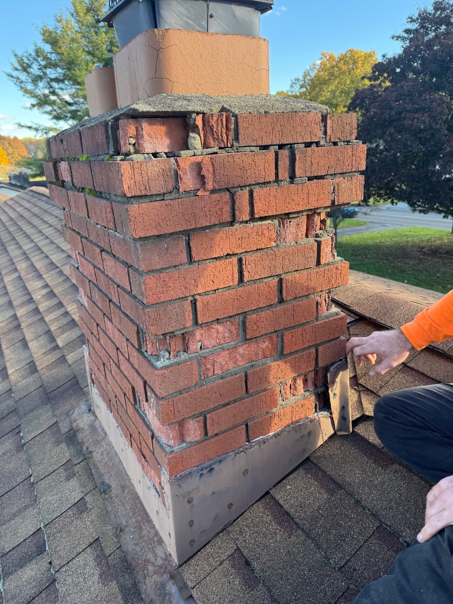 Mason's hand pointing to a crumbling mortar joint and failed flashing on a brick chimney